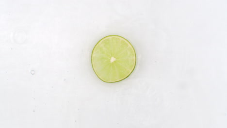 On-a-white-background-cut-into-slices-of-lime-sprinkled-with-water-spray.-Juicy-fresh-lime-in-slow-motion.